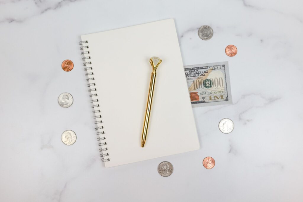 Cuaderno de espiral con bolígrafo y monedas que ilustra el registro manual del presupuesto con el método Kakeibo.