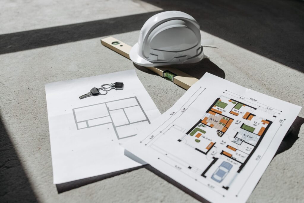 Planos de planta de una vivienda junto a un casco de obra blanca que representa proyectos de inversión en crowdfunding inmobiliario.
